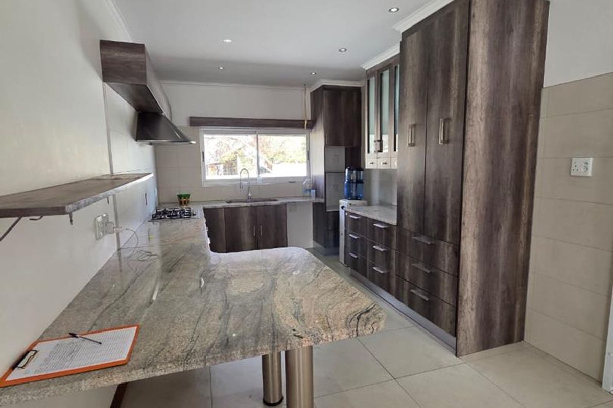 Modern kitchen featuring granite countertops, extensive built-in cabinetry, a gas hob, and a stainless steel extractor fan with neutral tiled flooring.