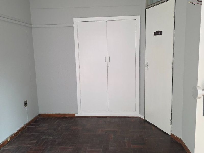 An empty bedroom featuring classic parquet flooring, a built-in cupboard, and a neutral wall finish, ready for personalization.