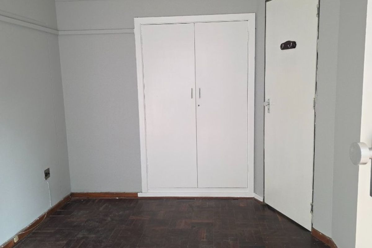 An empty bedroom featuring classic parquet flooring, a built-in cupboard, and a neutral wall finish, ready for personalization.