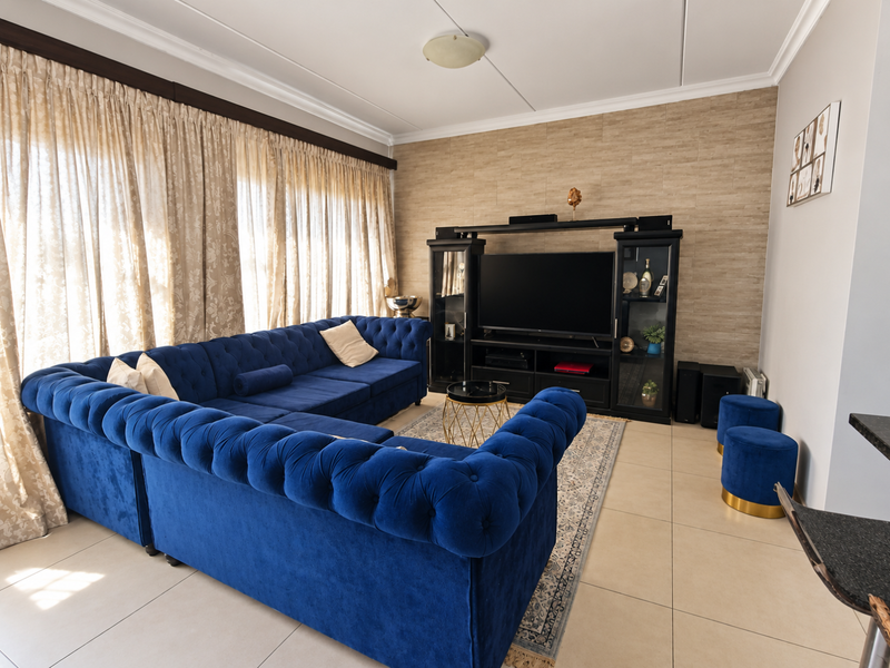 A well-maintained living room featuring large windows with curtain tracks, neutral tiled flooring, and a textured feature wall.