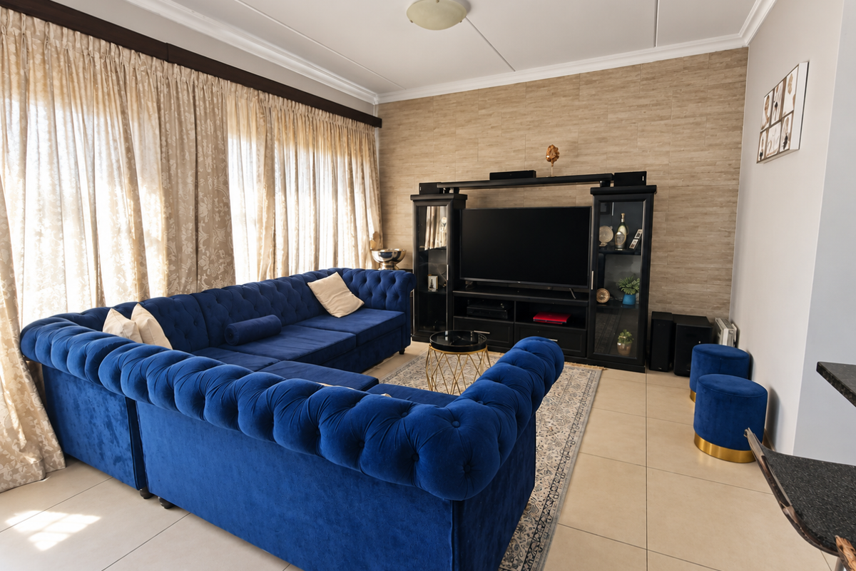 A well-maintained living room featuring large windows with curtain tracks, neutral tiled flooring, and a textured feature wall.