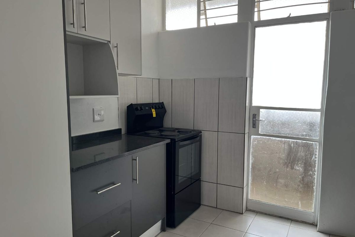A functional kitchen featuring dark cabinetry, stone countertops, a freestanding stove, and direct access to an outdoor area through a glass panel door.