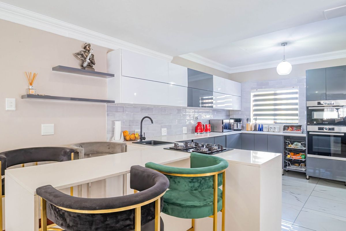 Modern kitchen featuring sleek high-gloss cabinetry, stone countertops, integrated gas hob, built-in oven, and stylish subway tile backsplash with a breakfast bar area.