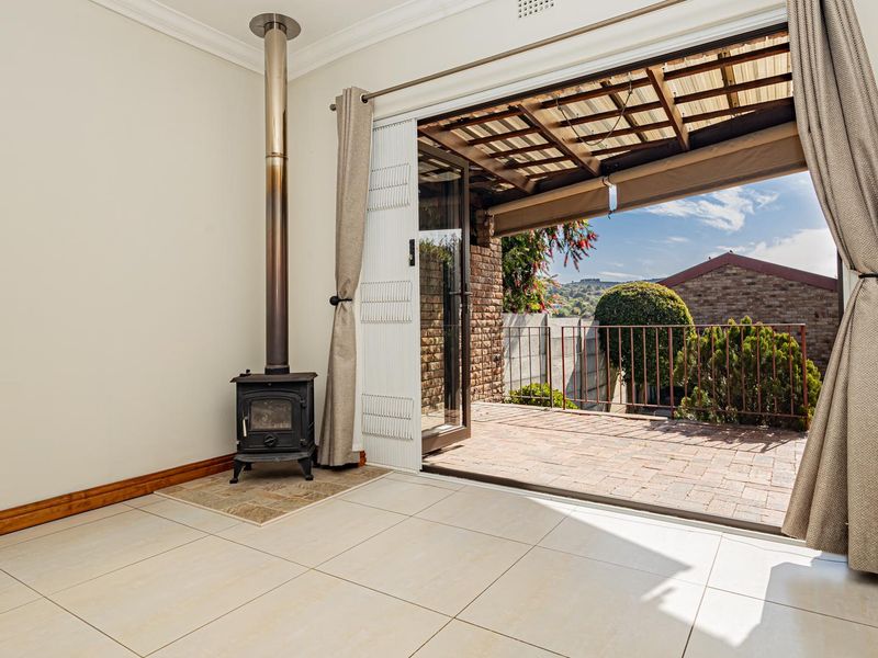 Bright living area featuring a freestanding fireplace and large sliding doors opening onto a covered brick-paved patio with outdoor views.