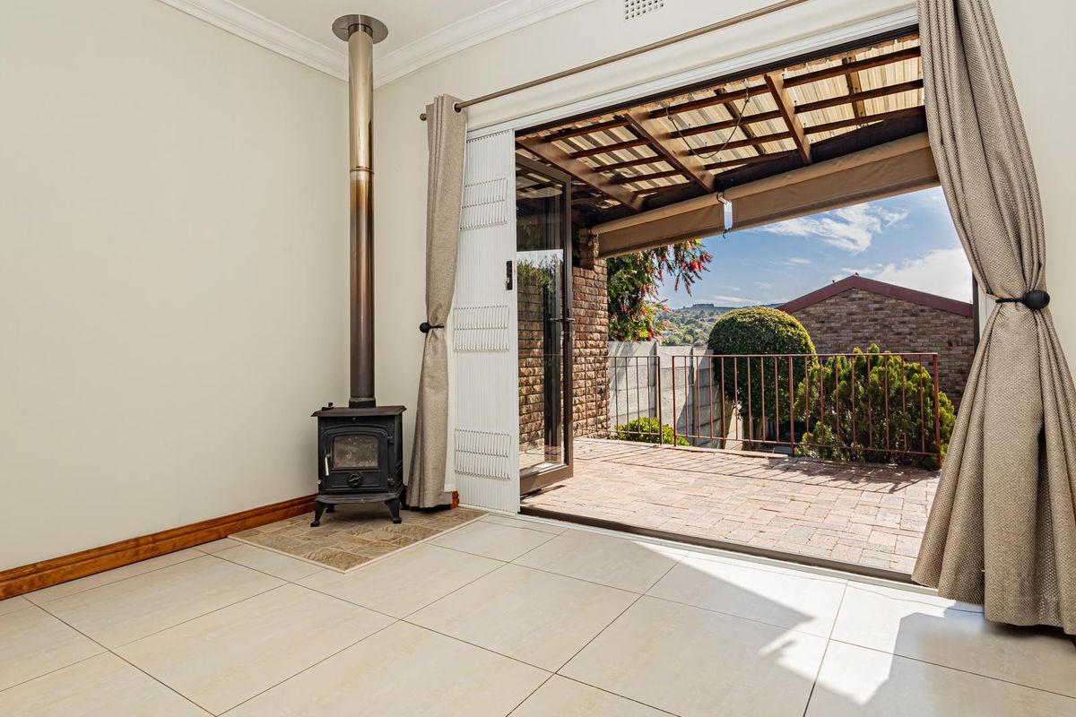 Bright living area featuring a freestanding fireplace and large sliding doors opening onto a covered brick-paved patio with outdoor views.