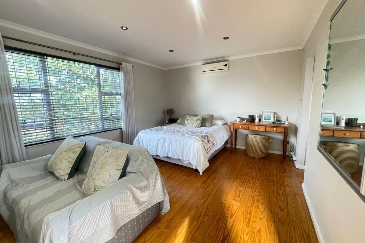 A spacious bedroom featuring polished hardwood flooring, recessed lighting, and a wall-mounted air conditioning unit, offering a comfortable and well-maintained living space.