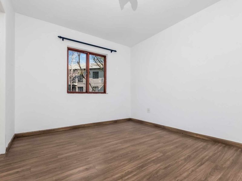 A bright, empty bedroom featuring modern laminate flooring, white walls, and a window with a curtain rod.