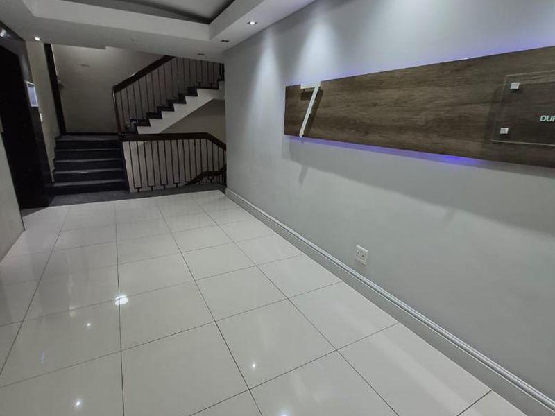 Modern office building entrance lobby featuring polished tile flooring, recessed ceiling lighting, and a contemporary staircase with metal railings.