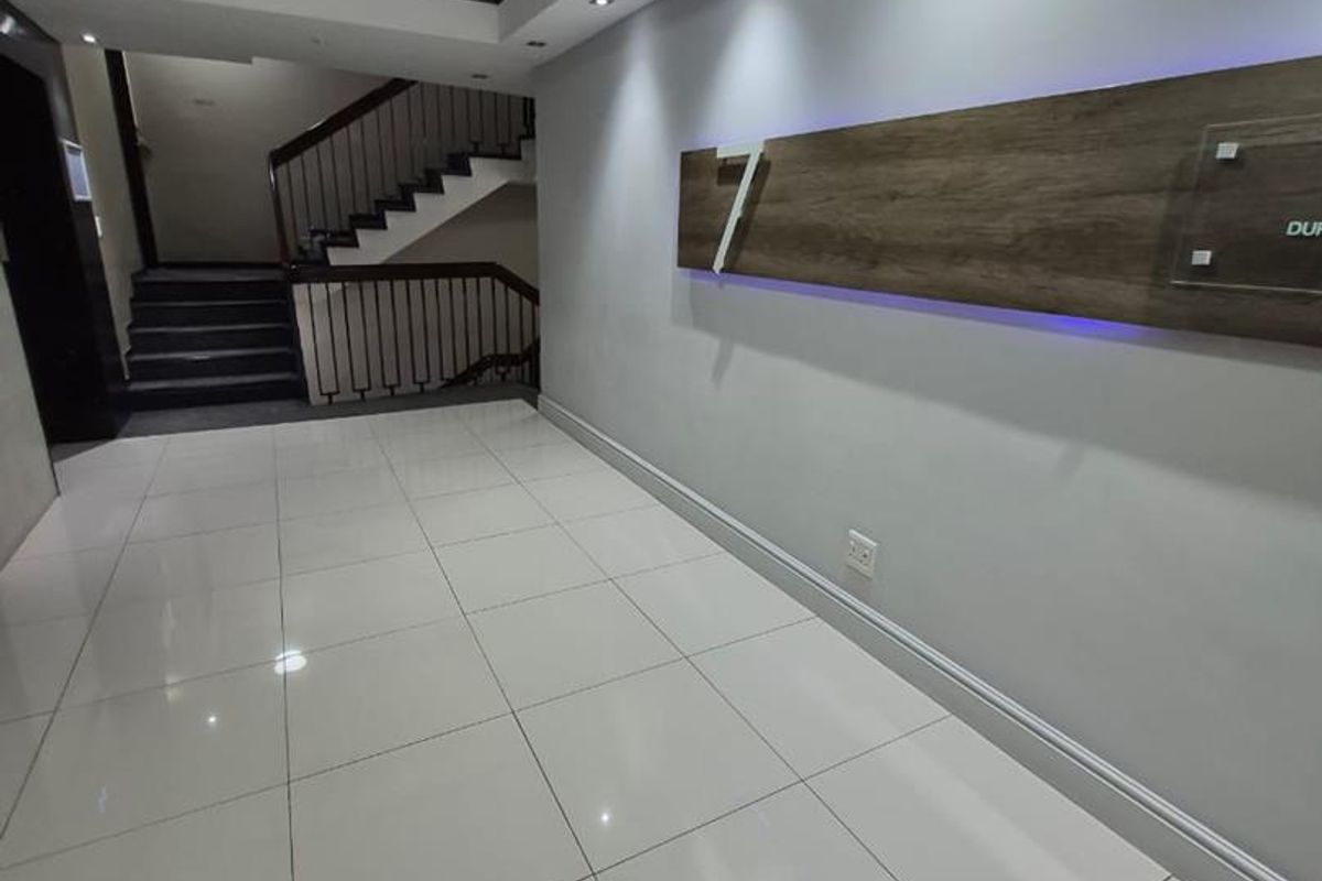 Modern office building entrance lobby featuring polished tile flooring, recessed ceiling lighting, and a contemporary staircase with metal railings.
