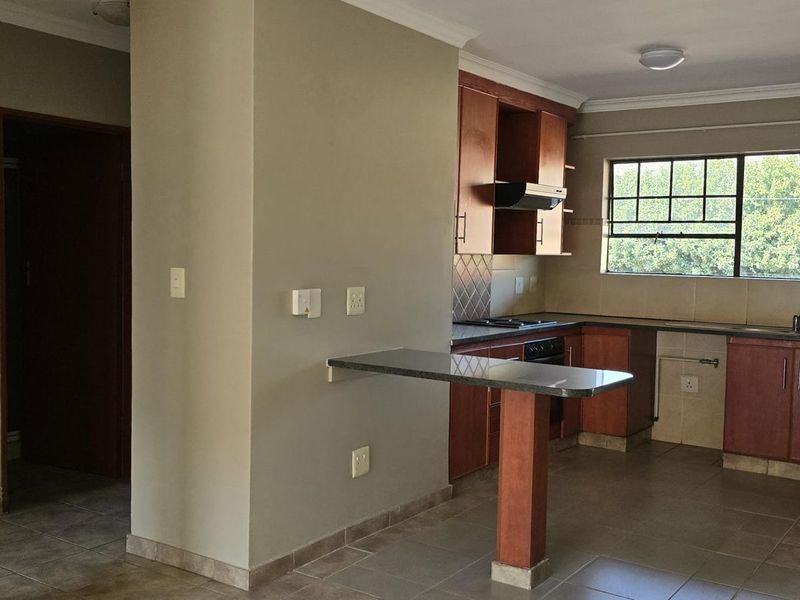 A functional kitchen featuring wooden cabinetry, a built-in hob and oven, a breakfast bar, and tiled flooring, with direct access to an outdoor balcony.