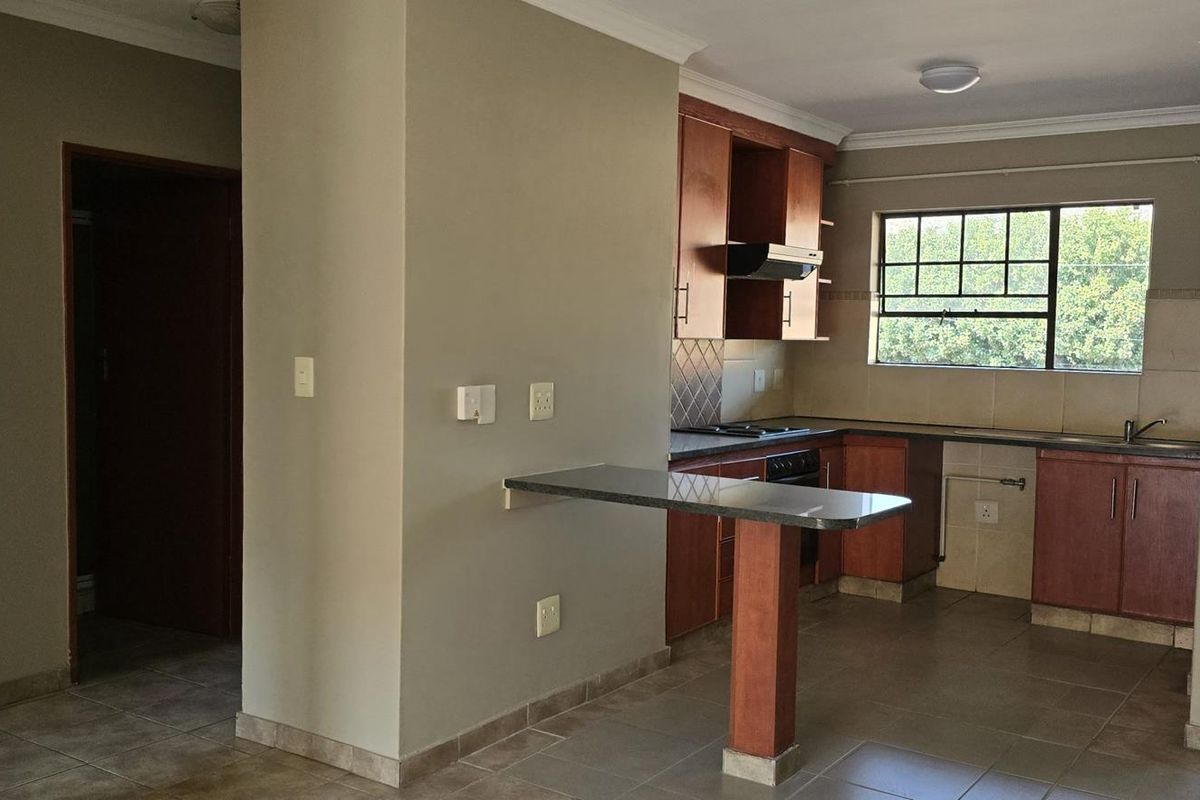 A functional kitchen featuring wooden cabinetry, a built-in hob and oven, a breakfast bar, and tiled flooring, with direct access to an outdoor balcony.