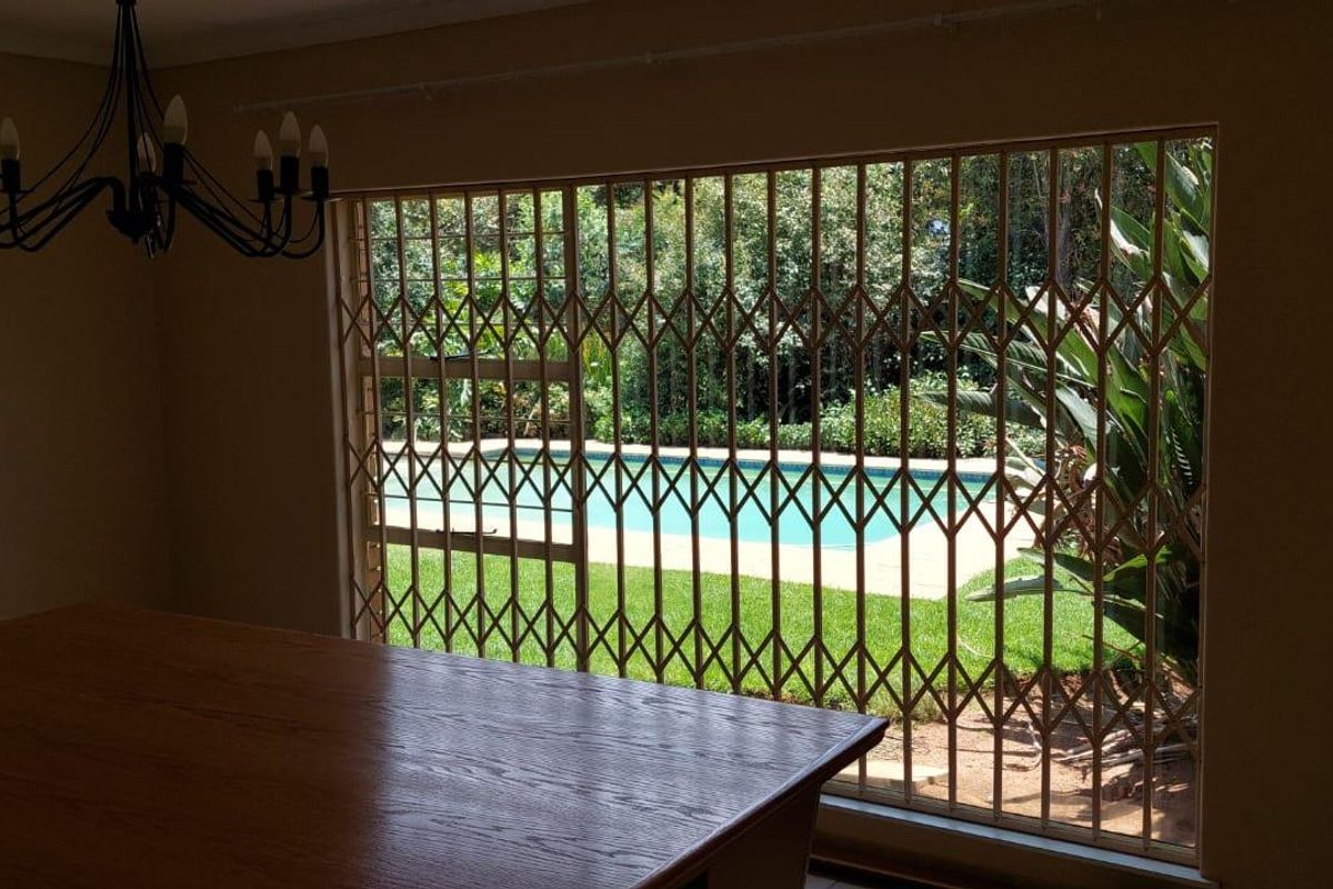 A living area featuring large windows with security gates, offering a view of the garden and swimming pool.