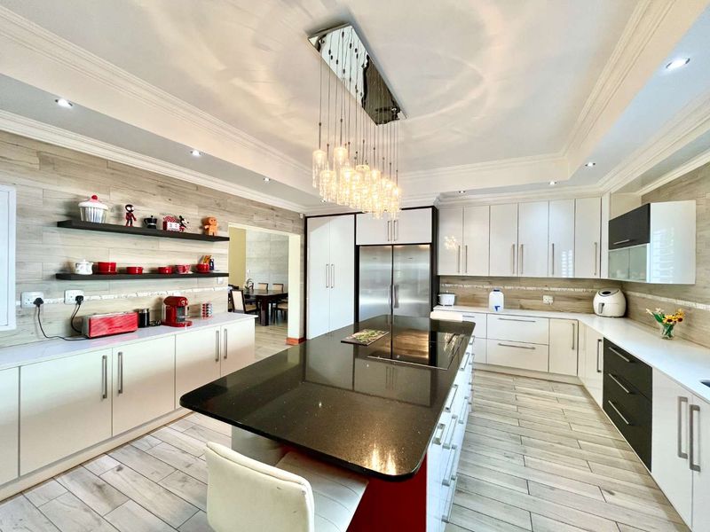 Modern kitchen featuring a large central island with granite countertops, sleek white and black cabinetry, integrated appliances, and stylish pendant lighting.