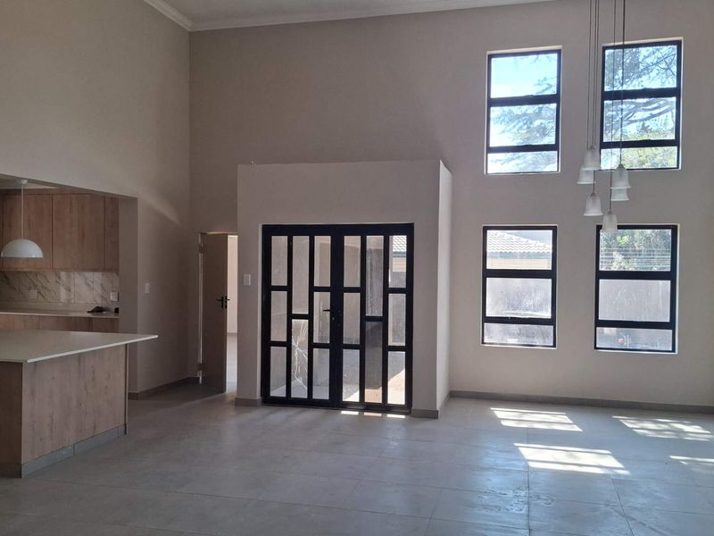 Spacious open-plan living area featuring double-height ceilings, large windows for natural light, and a modern kitchen with a central island and stone countertops.