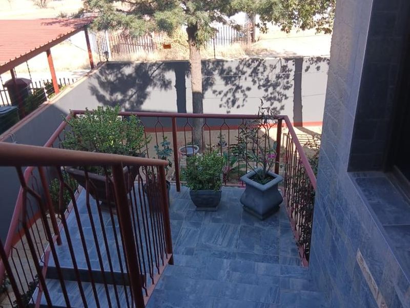 An elevated outdoor balcony featuring stone-look tiled stairs and a metal balustrade, overlooking a private garden area.