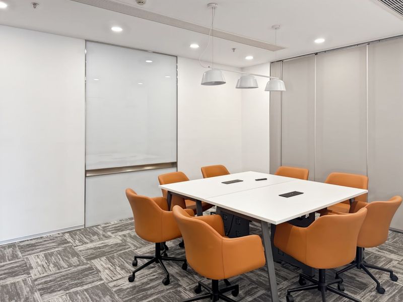 A modern, well-lit office meeting room featuring carpet tiles, a glass whiteboard, and a functional sliding partition wall for flexible space management.