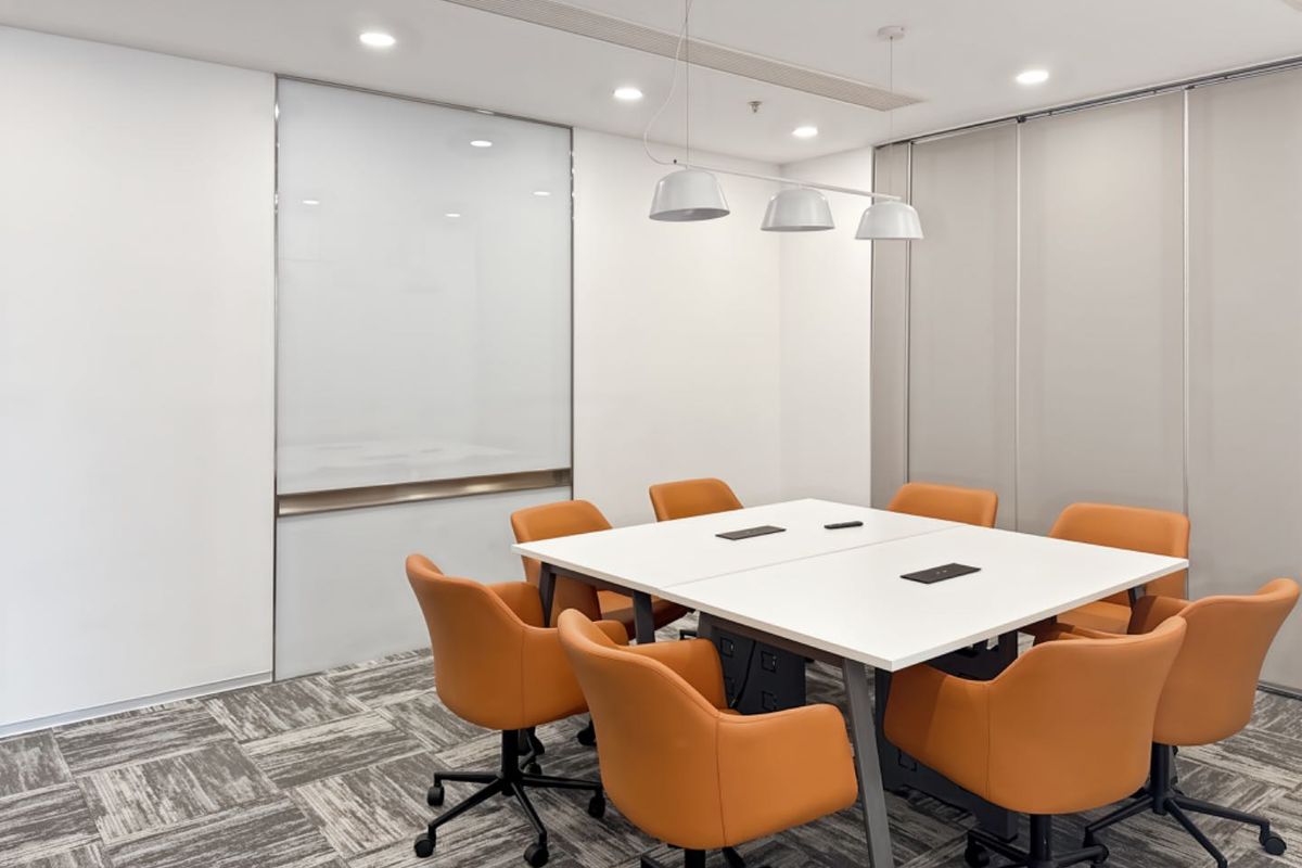 A modern, well-lit office meeting room featuring carpet tiles, a glass whiteboard, and a functional sliding partition wall for flexible space management.