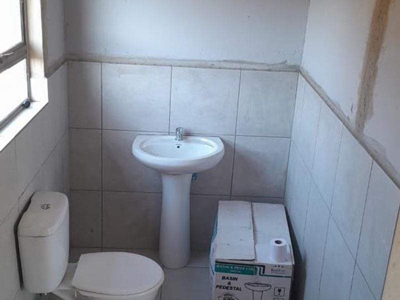 A small bathroom in the process of renovation, featuring a pedestal basin, toilet, and partially tiled walls requiring finishing touches.