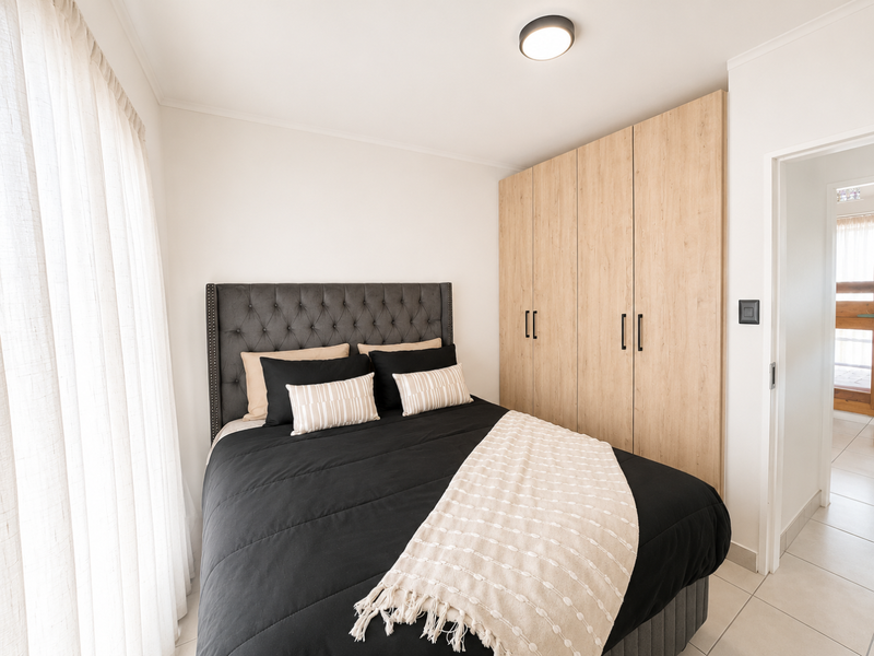 A well-maintained bedroom featuring light wood-finish built-in cupboards, neutral tiled flooring, and a modern flush mount ceiling light.