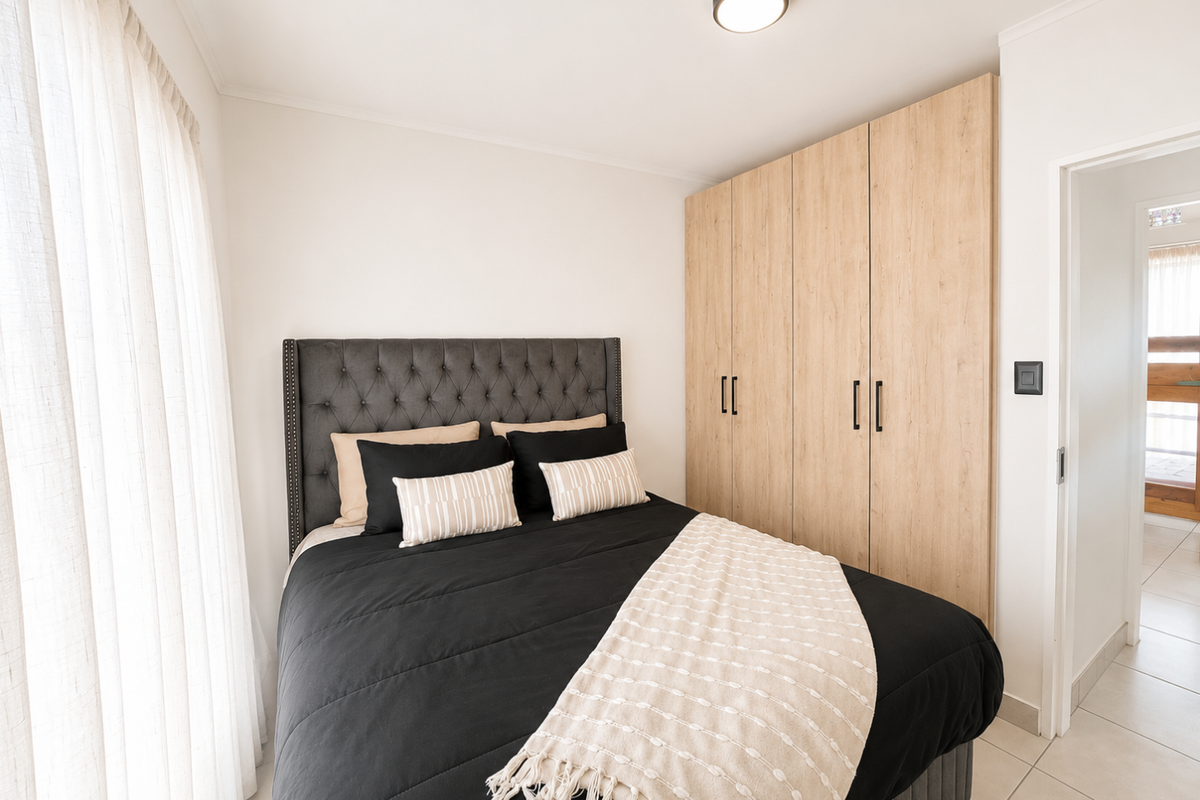 A well-maintained bedroom featuring light wood-finish built-in cupboards, neutral tiled flooring, and a modern flush mount ceiling light.