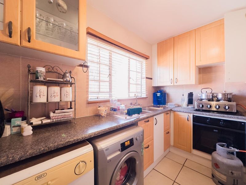 Functional kitchen featuring light wood cabinetry, granite-look countertops, built-in oven with gas hob, and tiled flooring with integrated laundry appliance space.