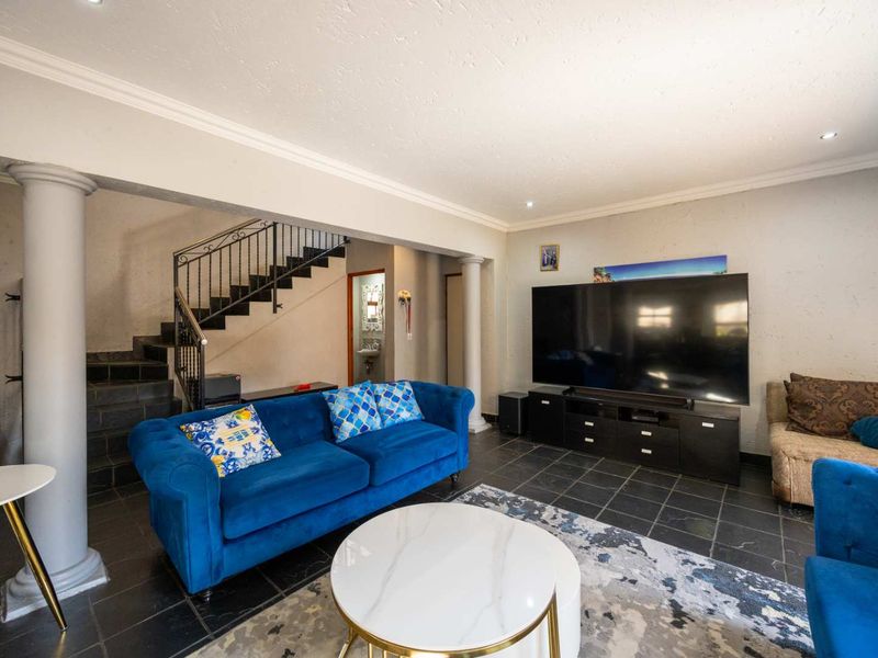 Spacious living room featuring dark stone floor tiles, decorative columns, and an open staircase with a wrought iron balustrade.