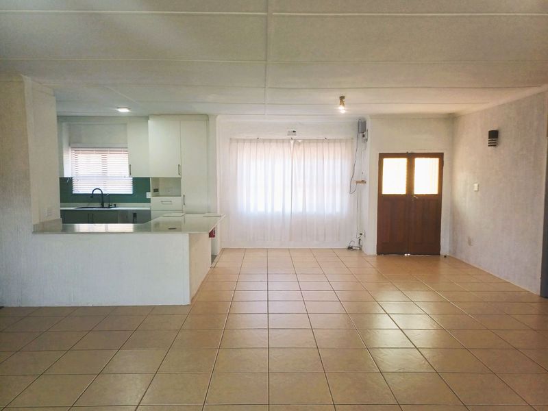 Spacious open-plan living area featuring tiled flooring, a functional kitchen with built-in cabinetry, and direct access through a timber entrance door.