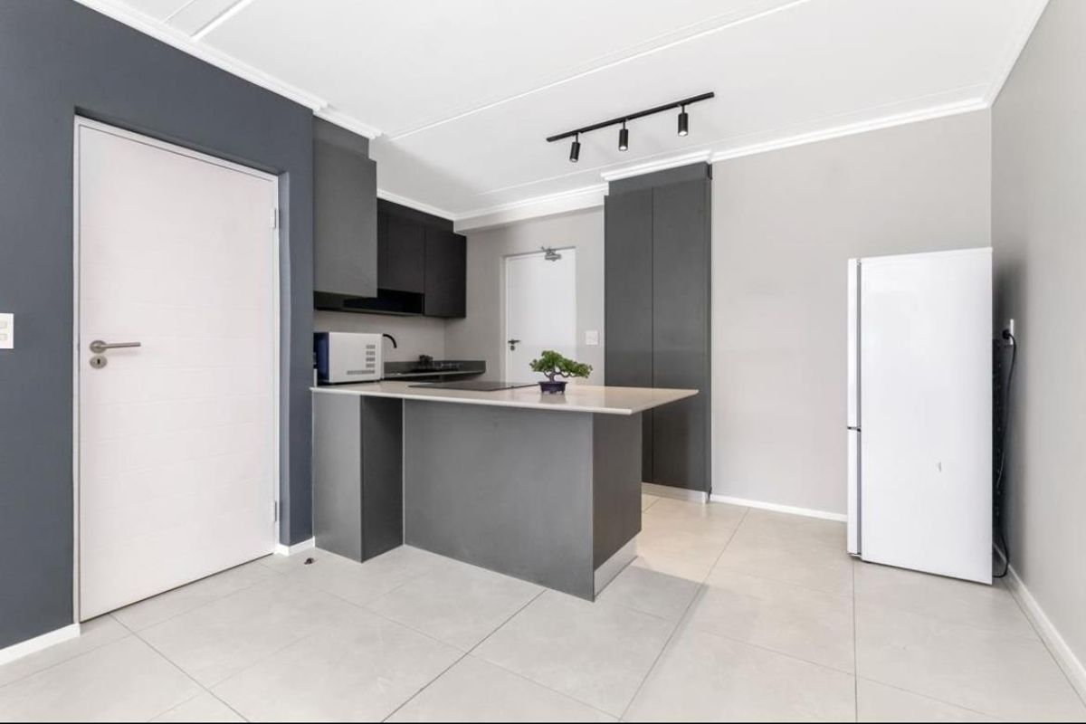 Modern kitchen featuring dark cabinetry, a central breakfast island, stone countertops, and sleek track lighting in an open-plan layout.