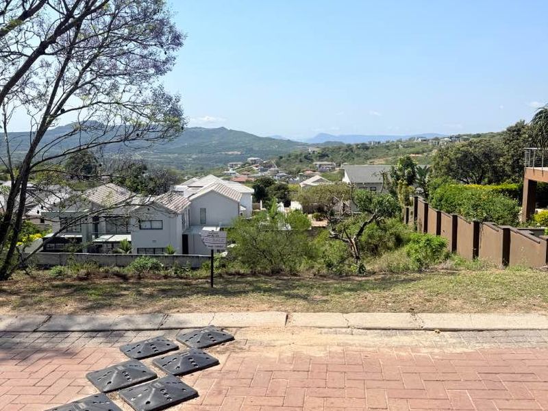 A scenic elevated view overlooking a residential estate with surrounding hills and landscape, captured from a paved driveway area.
