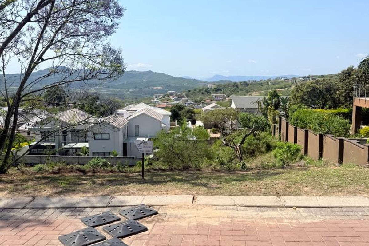 A scenic elevated view overlooking a residential estate with surrounding hills and landscape, captured from a paved driveway area.