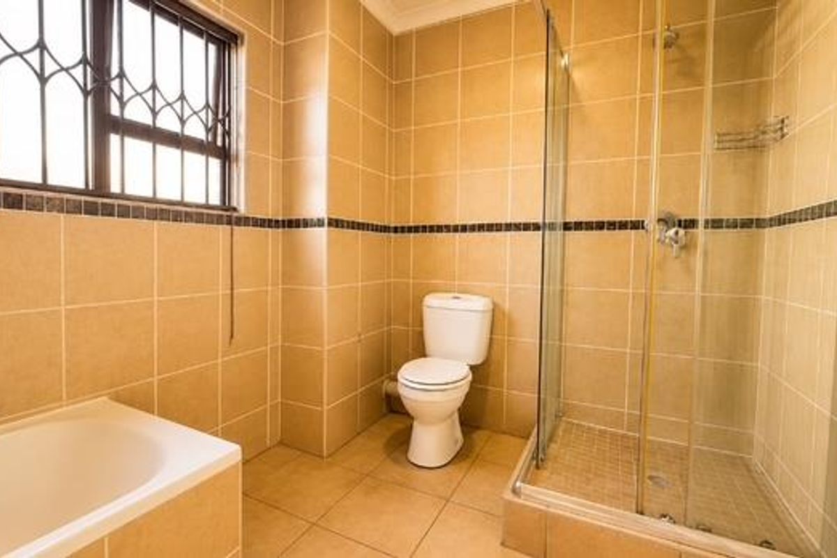 A functional bathroom featuring a built-in bathtub, a separate glass-enclosed shower, and neutral ceramic tiling throughout.