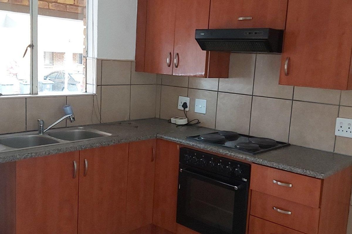 A functional kitchen featuring wooden cabinetry, a built-in oven with hob, extractor fan, and a double-basin sink with tiled backsplash.