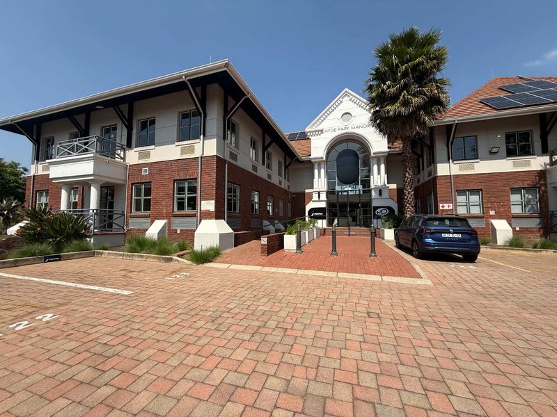 Front exterior view of Hyde Park Manor office building featuring brick facade, tiled roof with solar panels, and paved parking area.