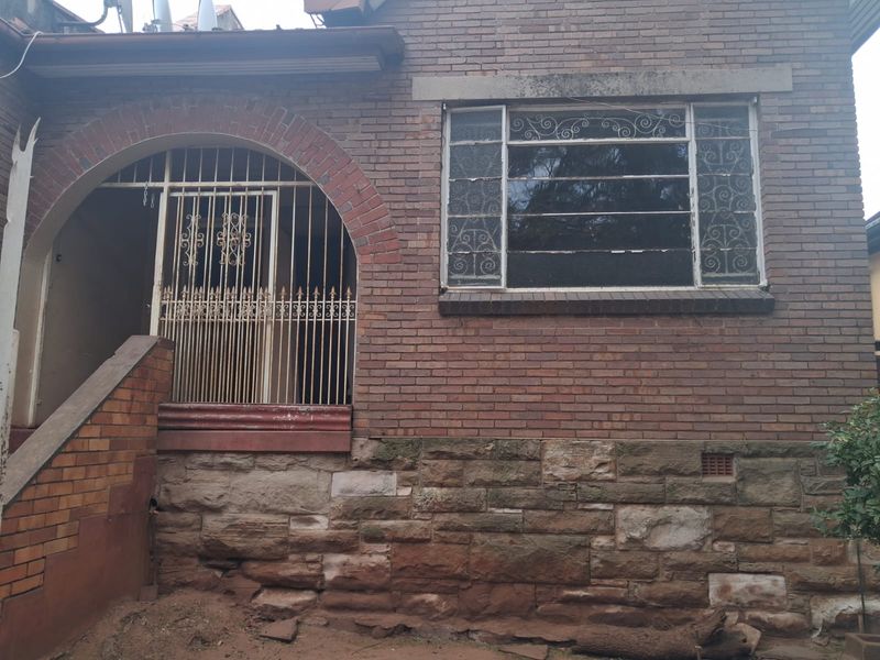 Front elevation of a brick house featuring a stone foundation, arched entrance with security gate, and classic multi-pane windows with security bars.