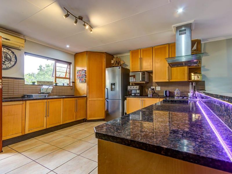 A functional kitchen featuring wooden cabinetry, granite countertops, a breakfast bar with integrated lighting, and tiled flooring.