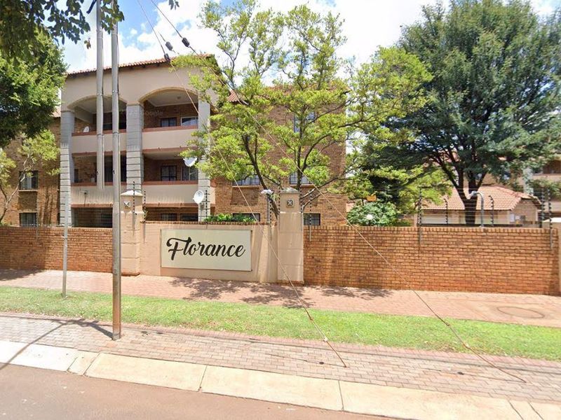 Street view of the Florance apartment complex featuring a brick boundary wall, electric fencing, and multi-story residential units with balconies.