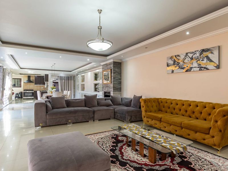 Spacious open-plan living area featuring tiled floors, a stone-clad fireplace, built-in cabinetry, and elegant recessed ceiling details with integrated lighting.