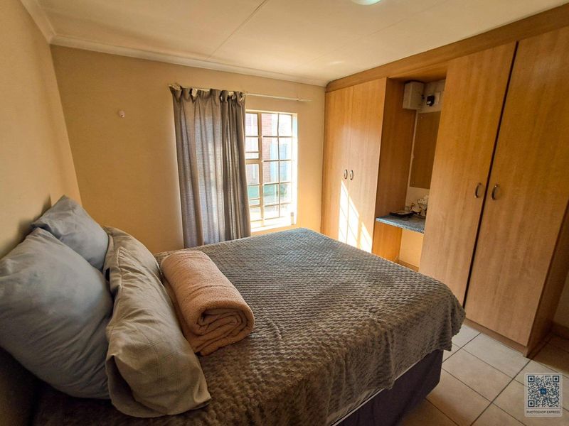 A functional bedroom featuring built-in wooden wardrobes with an integrated vanity area and tiled flooring.