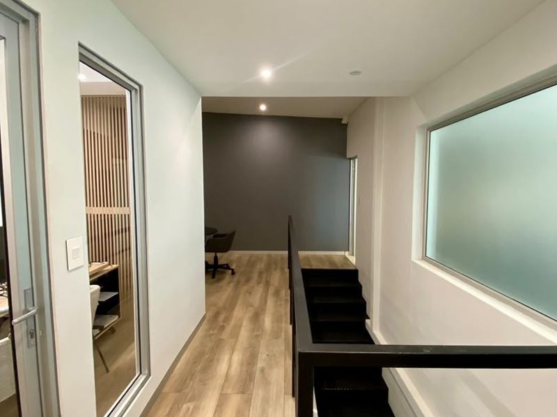 A modern, well-lit hallway featuring laminate flooring, a sleek metal staircase with a handrail, and a recessed ceiling air conditioning unit.
