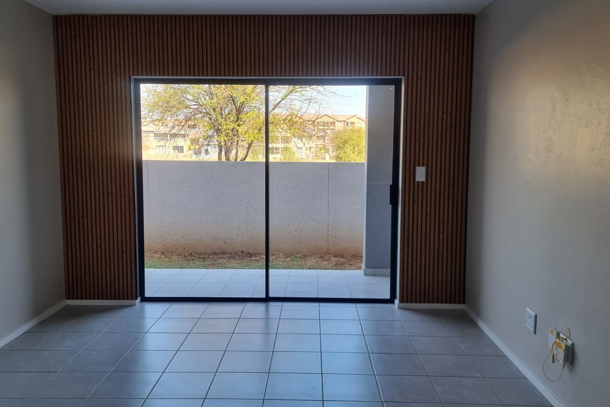 An empty living room featuring modern slatted wood wall paneling, neutral tiled flooring, and a large sliding glass door providing access to the exterior.