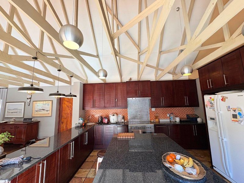 Spacious kitchen featuring dark wood cabinetry, granite countertops, mosaic backsplash, and a striking exposed timber truss ceiling with modern pendant lighting.