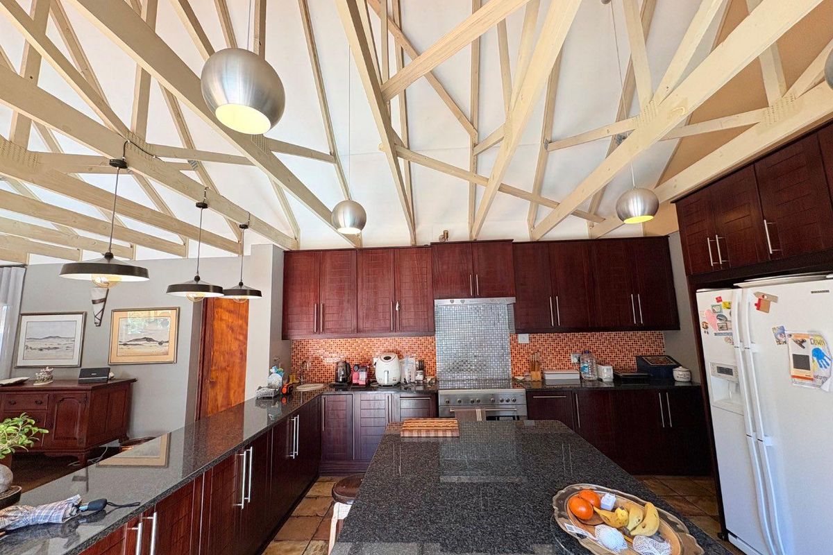 Spacious kitchen featuring dark wood cabinetry, granite countertops, mosaic backsplash, and a striking exposed timber truss ceiling with modern pendant lighting.