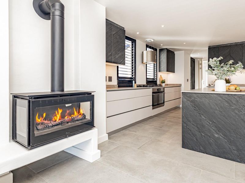 Modern open-plan kitchen and living area featuring a sleek fireplace, stone-topped island, built-in appliances, and contemporary cabinetry with recessed lighting.