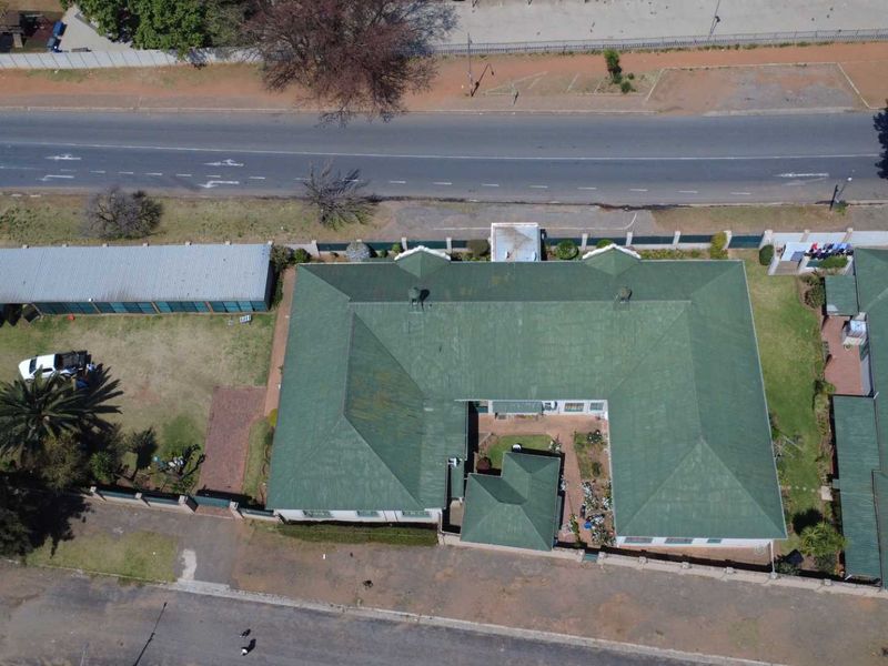 Aerial view of the property showing the main house with a green pitched roof, surrounding garden, perimeter wall, and detached outbuilding.