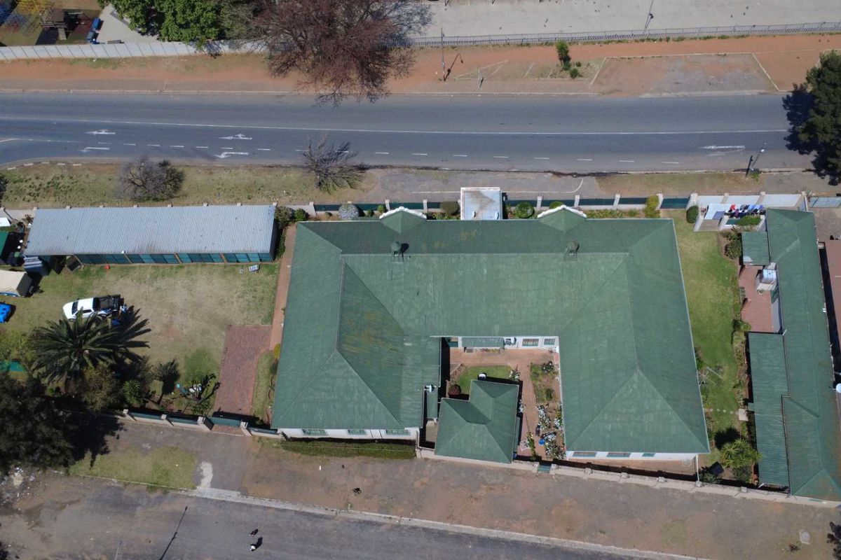 Aerial view of the property showing the main house with a green pitched roof, surrounding garden, perimeter wall, and detached outbuilding.