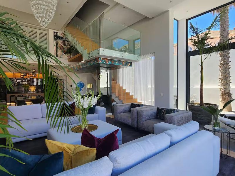 Spacious open-plan living area featuring double-volume ceilings, a modern glass-railed staircase, and expansive floor-to-ceiling windows providing abundant natural light.
