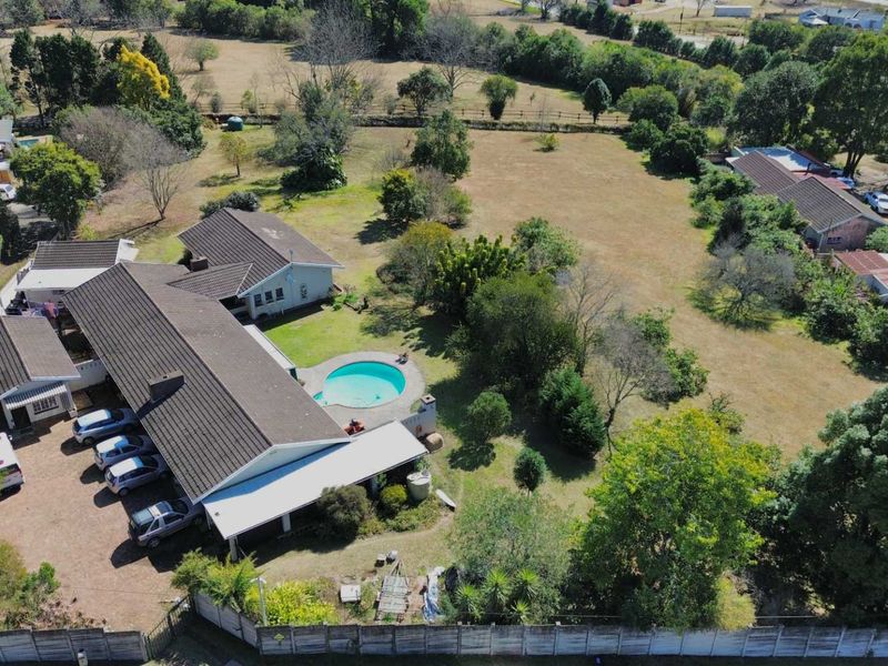 Aerial view of a residential property featuring a large garden, swimming pool, covered patio, and ample driveway space on a spacious plot.
