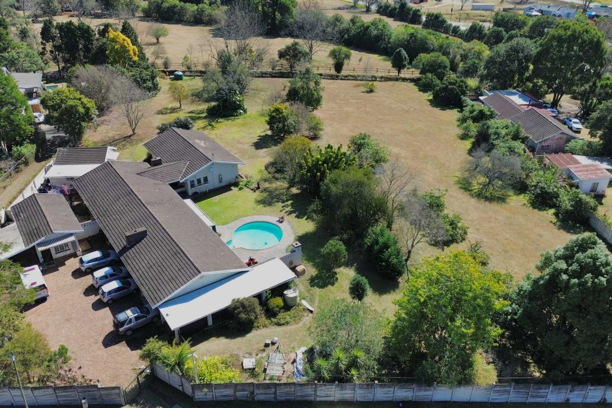 Aerial view of a residential property featuring a large garden, swimming pool, covered patio, and ample driveway space on a spacious plot.