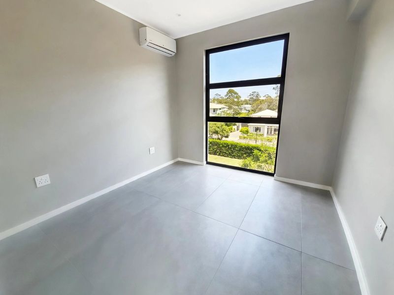 A bright, modern, and empty bedroom featuring large format floor tiles, a split-system air conditioner, and a large window with a pleasant neighbourhood view.