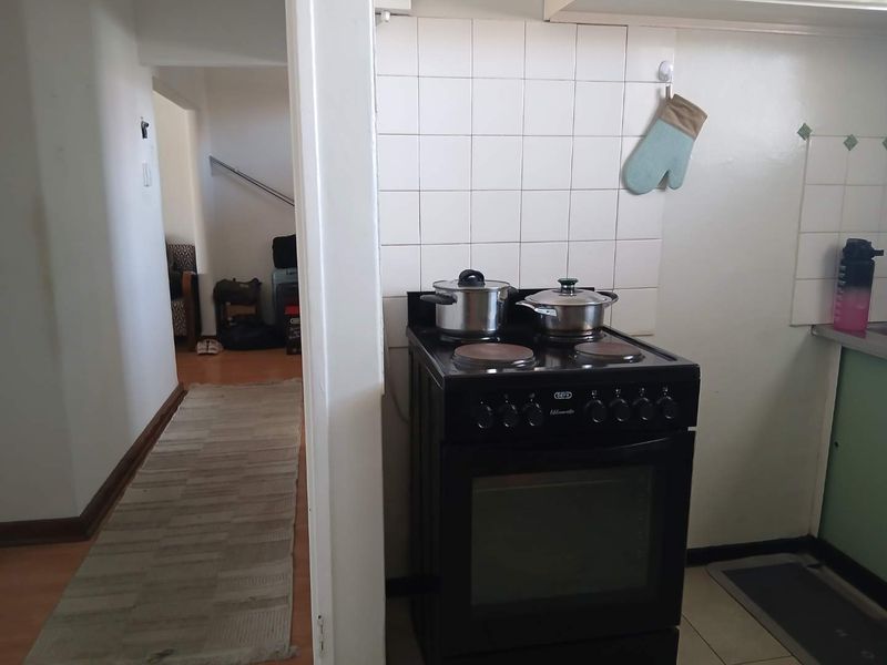 A compact kitchen area featuring a freestanding electric stove and tiled splashback, leading into a hallway with laminate flooring.